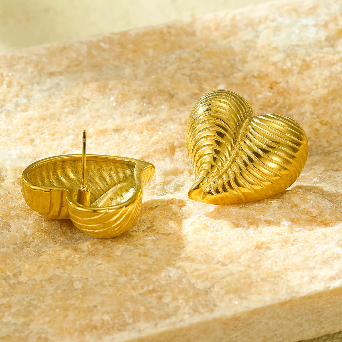 Back view of striped heart earrings showing the gold pin post, displayed on textured beige stone