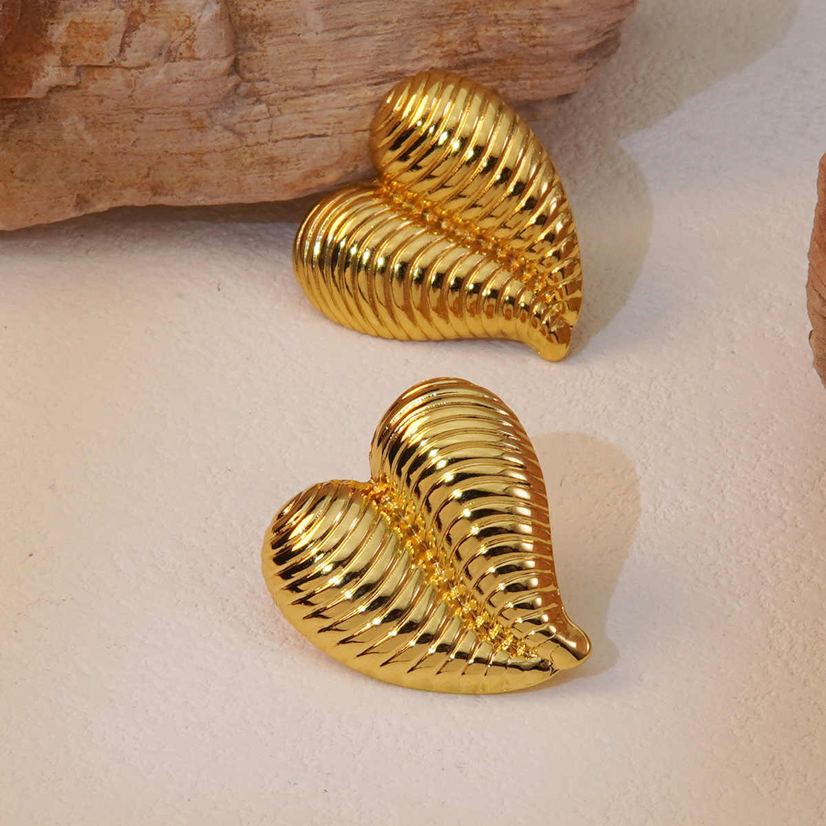 Shiny gold heart earrings placed on a textured off-white background with rustic stone elements