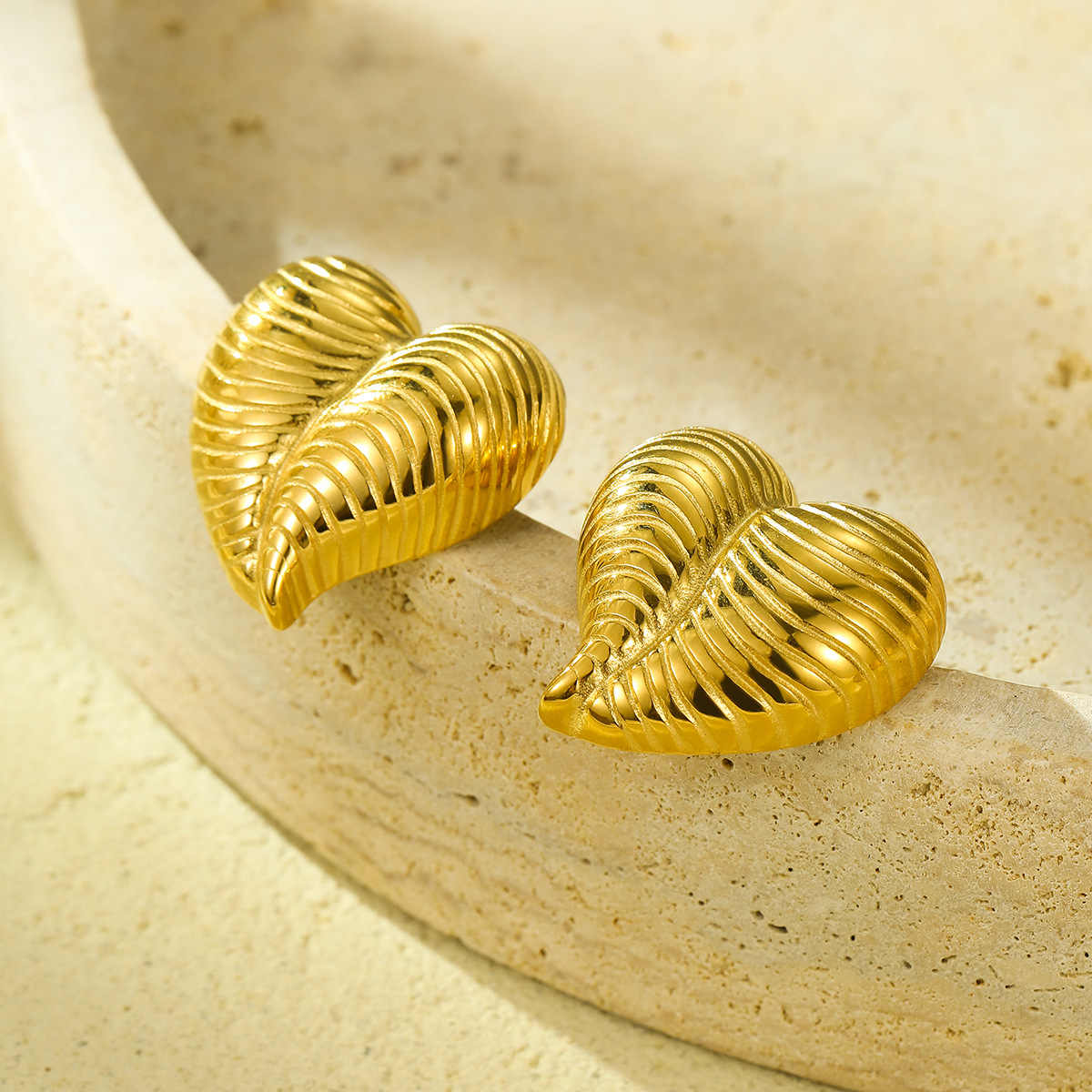Gold textured heart earrings resting on the edge of a stone bowl, catching natural light