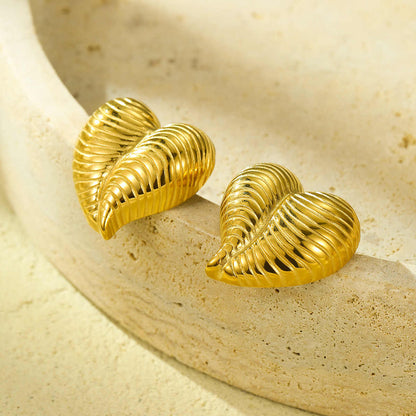 Gold textured heart earrings resting on the edge of a stone bowl, catching natural light