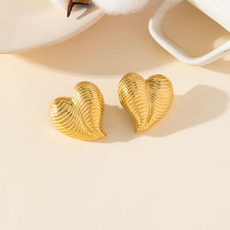 Minimalist gold heart shell earrings placed beside a cotton stem and white ceramic dish on a neutral surface