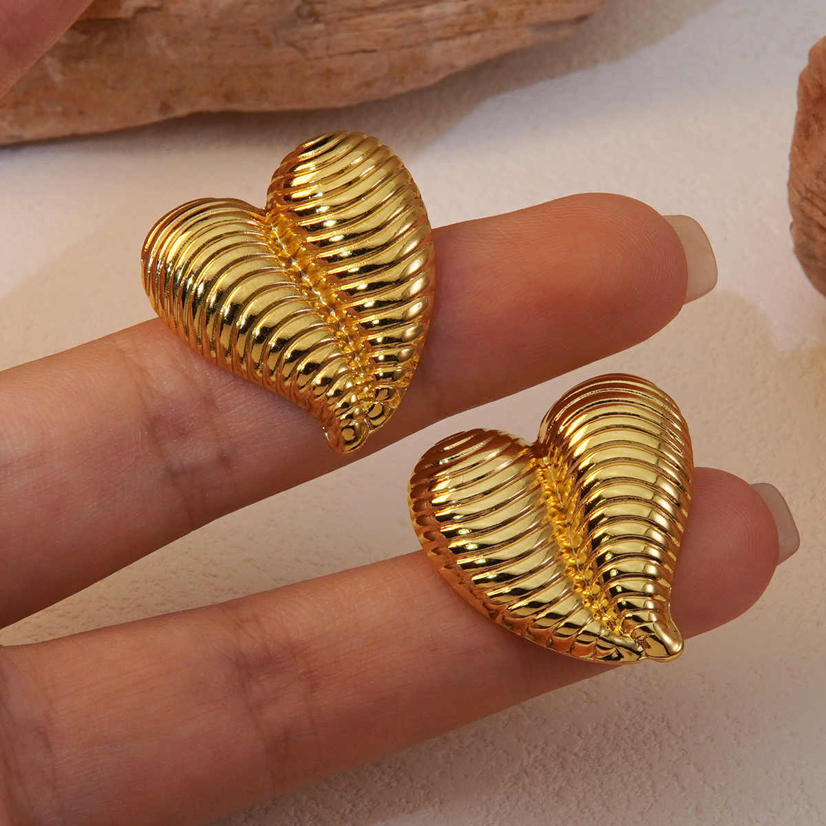 Close-up of gold heart-shaped ribbed earrings held on fingertips showing their reflective texture and size