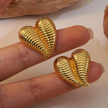 Close-up of gold heart-shaped ribbed earrings held on fingertips showing their reflective texture and size
