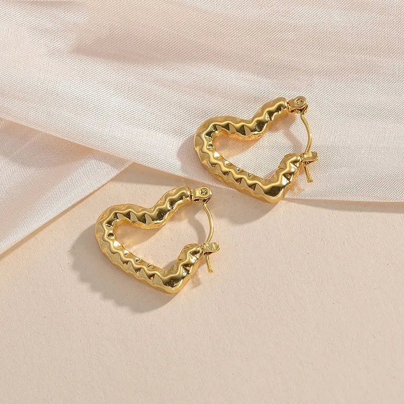 Wavy gold-toned heart earrings placed on peach and satin background.