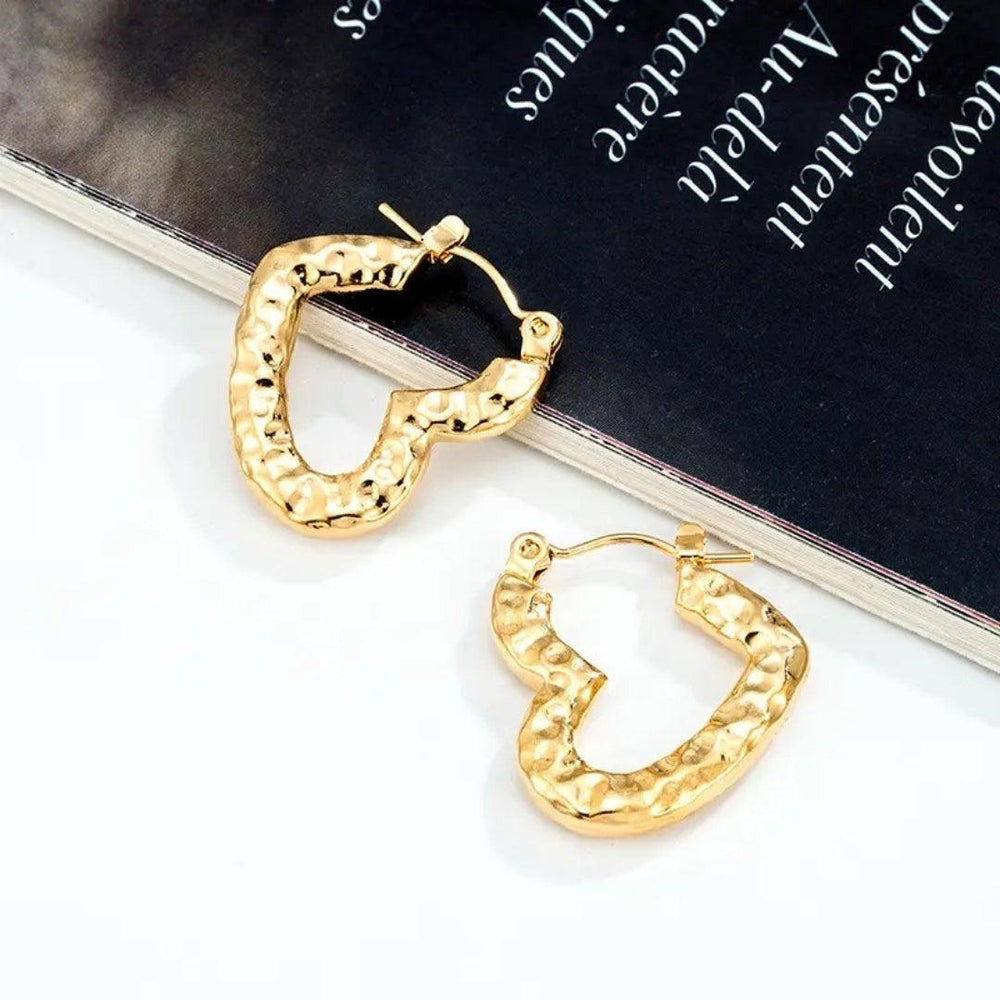 Hammered gold heart hoop earrings placed over a black magazine with white text.