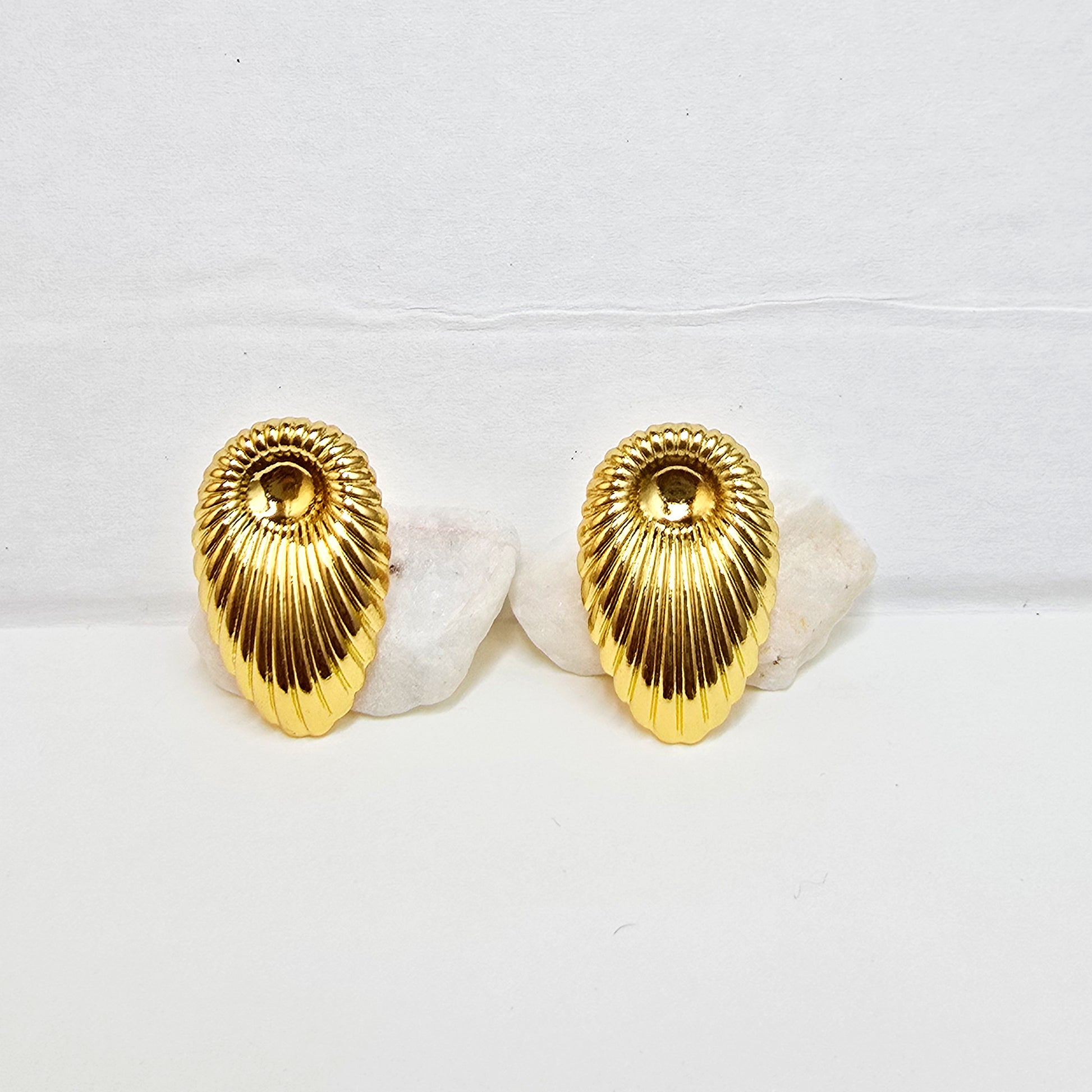 A pair of high-polish gold ribbed shell-shaped stud earrings displayed flat on a white background.