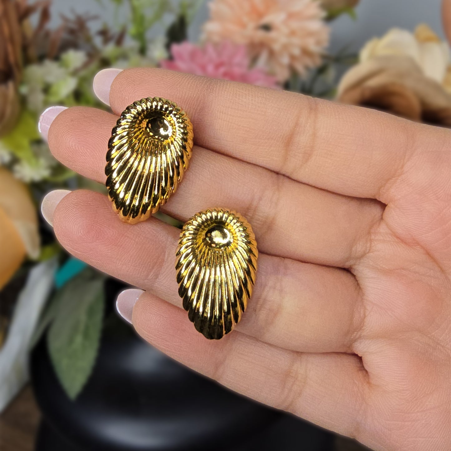 A hand holding two large gold fluted shell earrings to show the reflective shine and scale of the pieces.