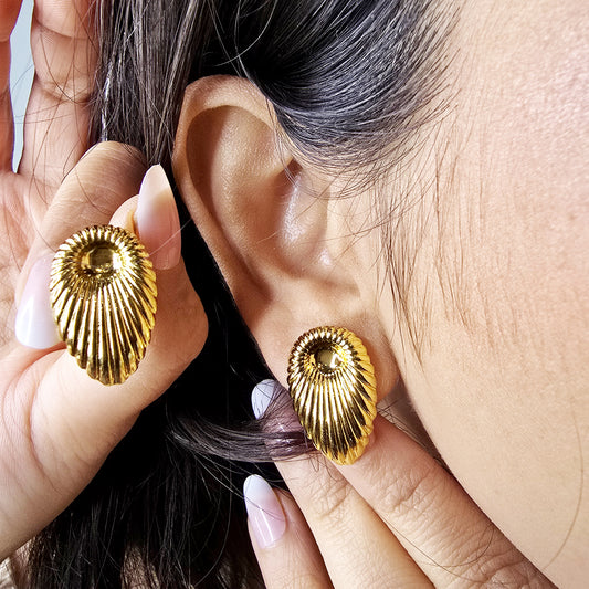 Side-view macro shot of a model wearing a gold ribbed shell earring, showcasing the vintage fan-style silhouette.