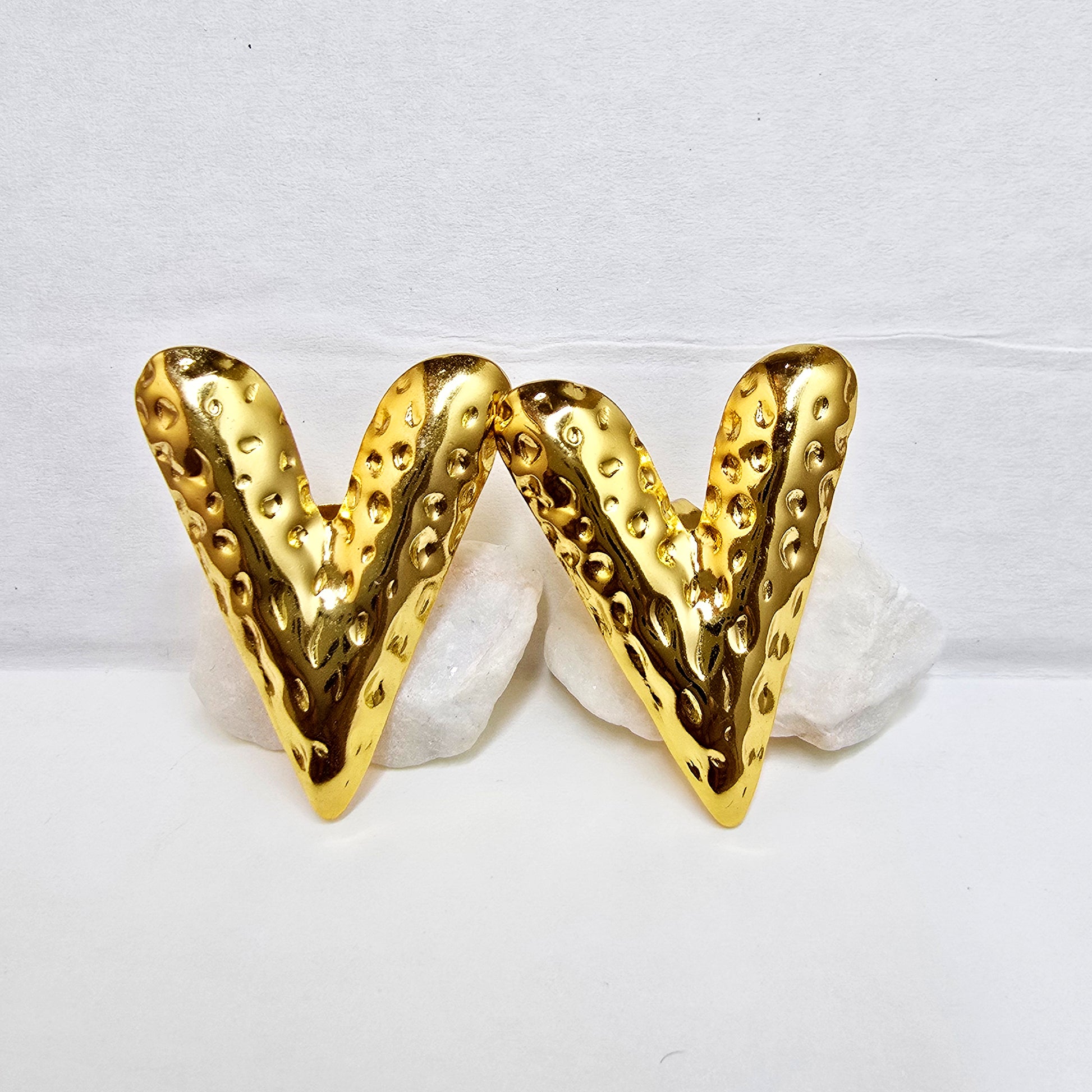 A pair of gold-plated V-shaped stud earrings with a deep hammered texture displayed on white rocks.