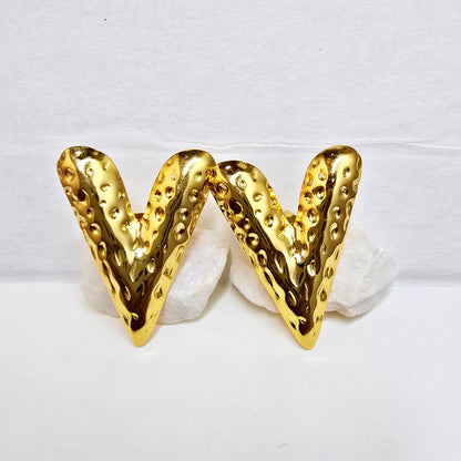 A pair of gold-plated V-shaped stud earrings with a deep hammered texture displayed on white rocks.