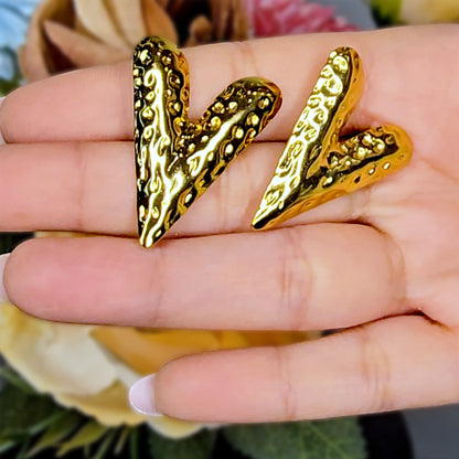 Close-up of bold hammered gold V earrings held in a hand to show the reflective texture and large sculptural scale.
