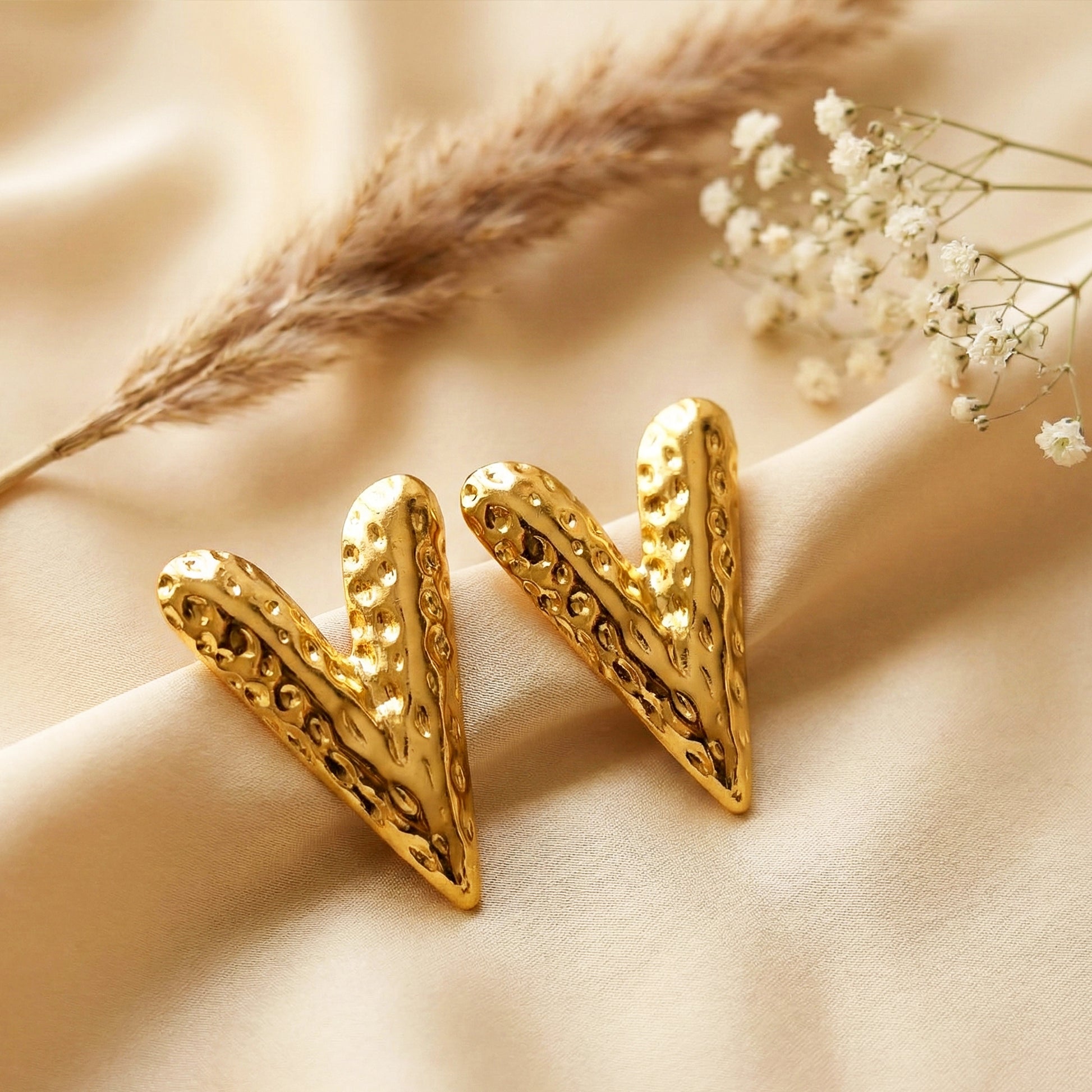Aesthetic lifestyle photography of gold V earrings on a beige silk cloth with dried floral accents.