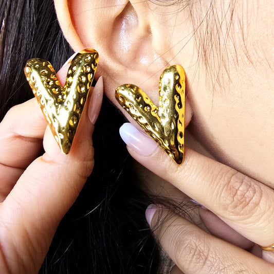 Side profile macro shot of a model wearing a gold hammered V stud earring, showcasing the bold geometric silhouette.