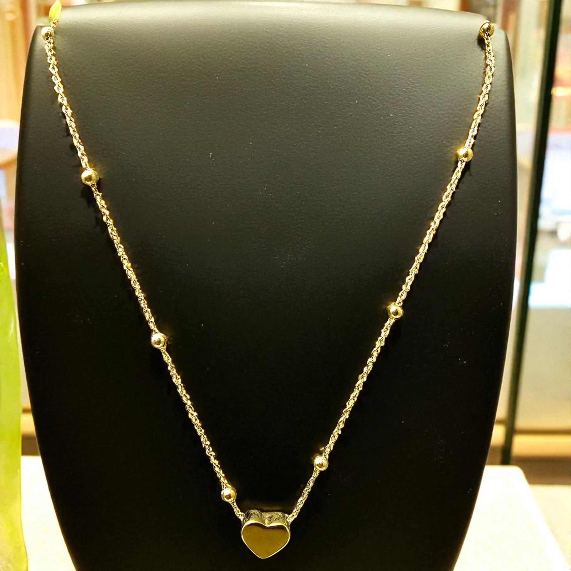 Necklace on black jewelry stand showing dainty design and polished heart pendant.