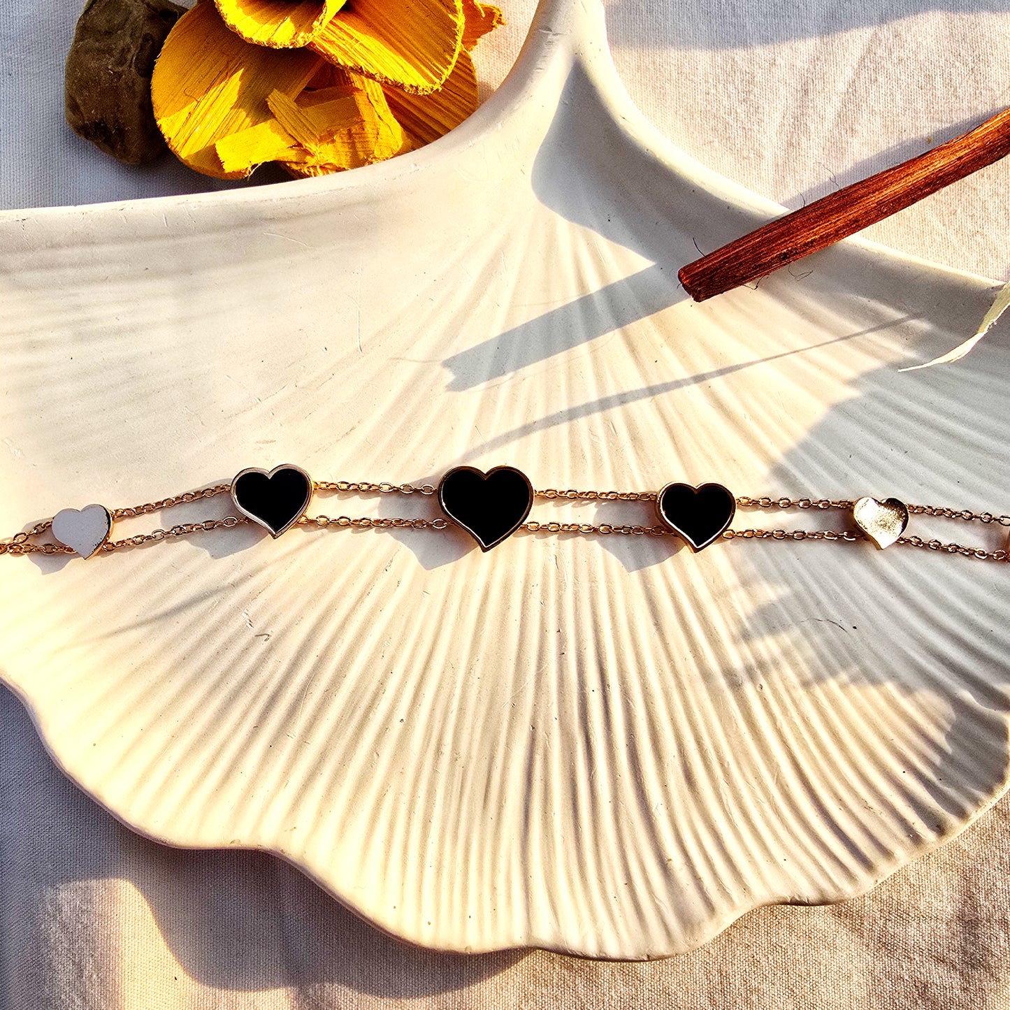 Aesthetic flat lay of the dainty black heart bracelet on a white shell tray.