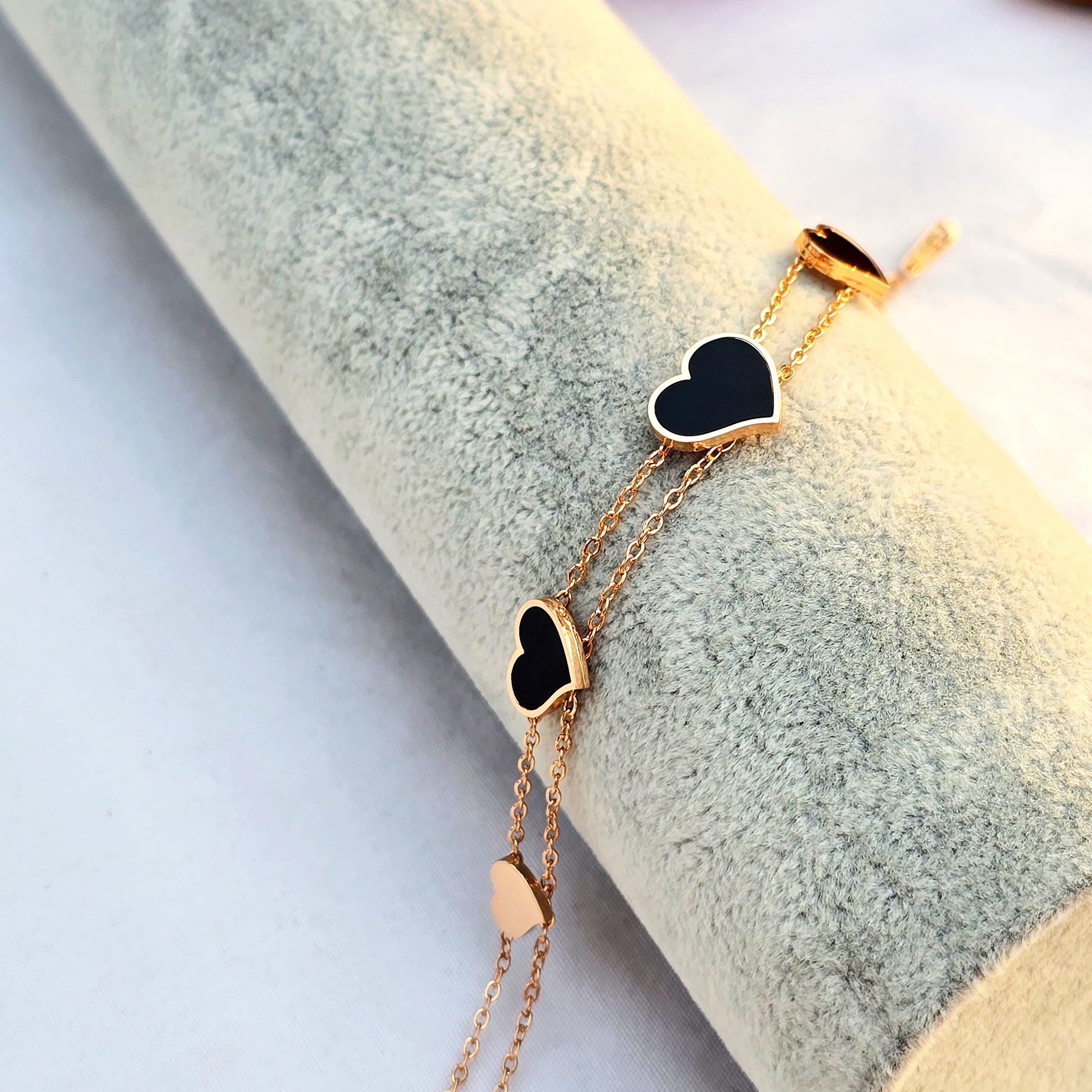 Side profile of gold heart bracelet showing the spacing of the five black hearts.