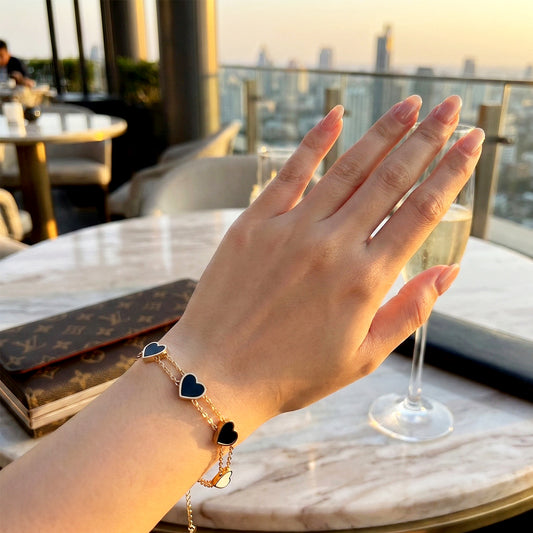 Woman’s wrist wearing a delicate gold chain bracelet with small black heart charms.