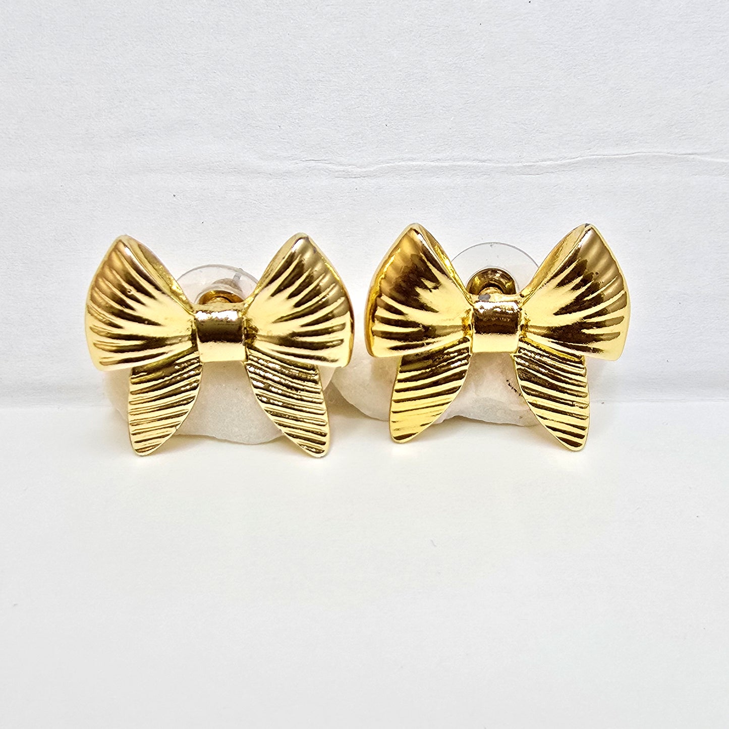 A pair of high-polish gold ribbed bow-shaped stud earrings displayed flat on a white background.