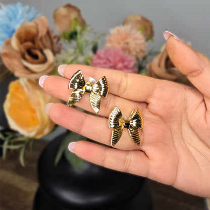 Close-up of gold Honey Bow earrings held in a hand to show the reflective ribbed texture and delicate ribbon design.