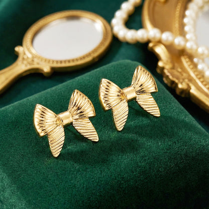 Aesthetic photography of gold bow earrings on a deep green velvet box with a pearl necklace and vintage mirror.