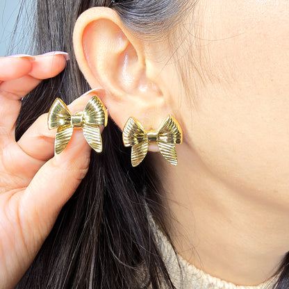 Macro shot of a model wearing the gold Honey Bow earrings, highlighting the scale and ribbed finish against the earlobe.
