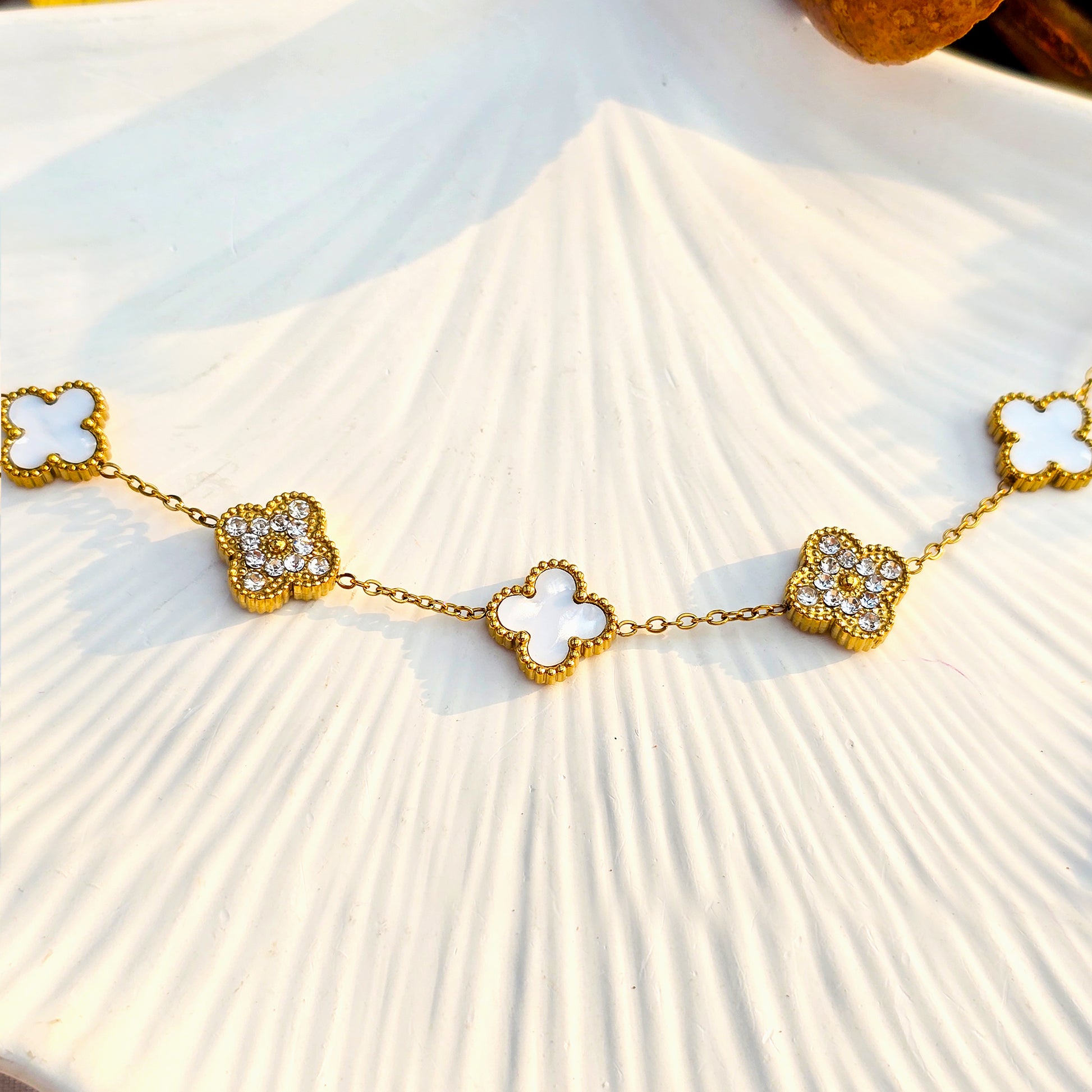 Gold anti-tarnish bracelet with alternating white shell and crystal pave clover motifs on white texture.
