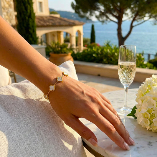 Woman wearing luxury gold clover bracelet styled with white floral background.