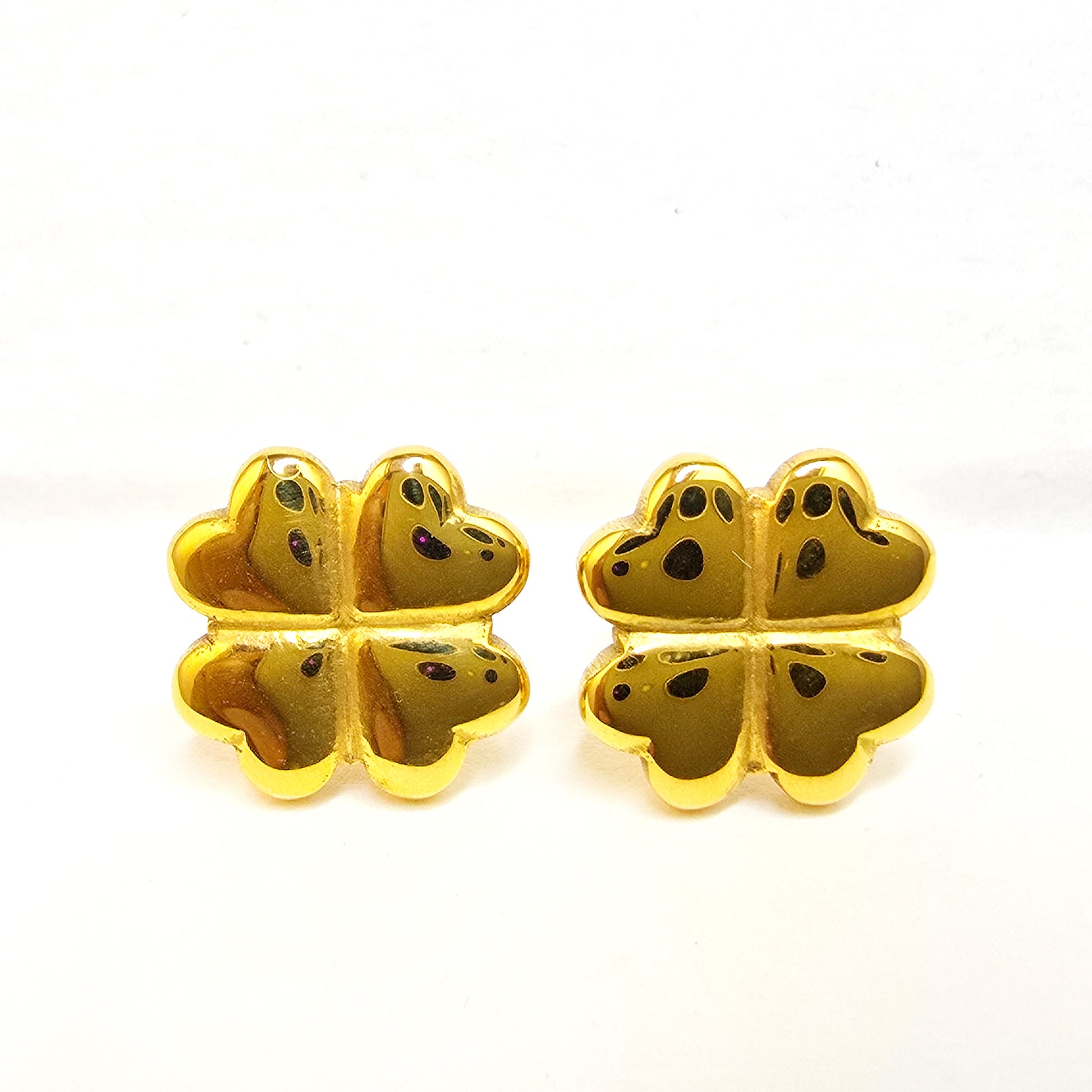 A pair of high-polish 18k gold-plated clover stud earrings displayed on white decorative rocks.