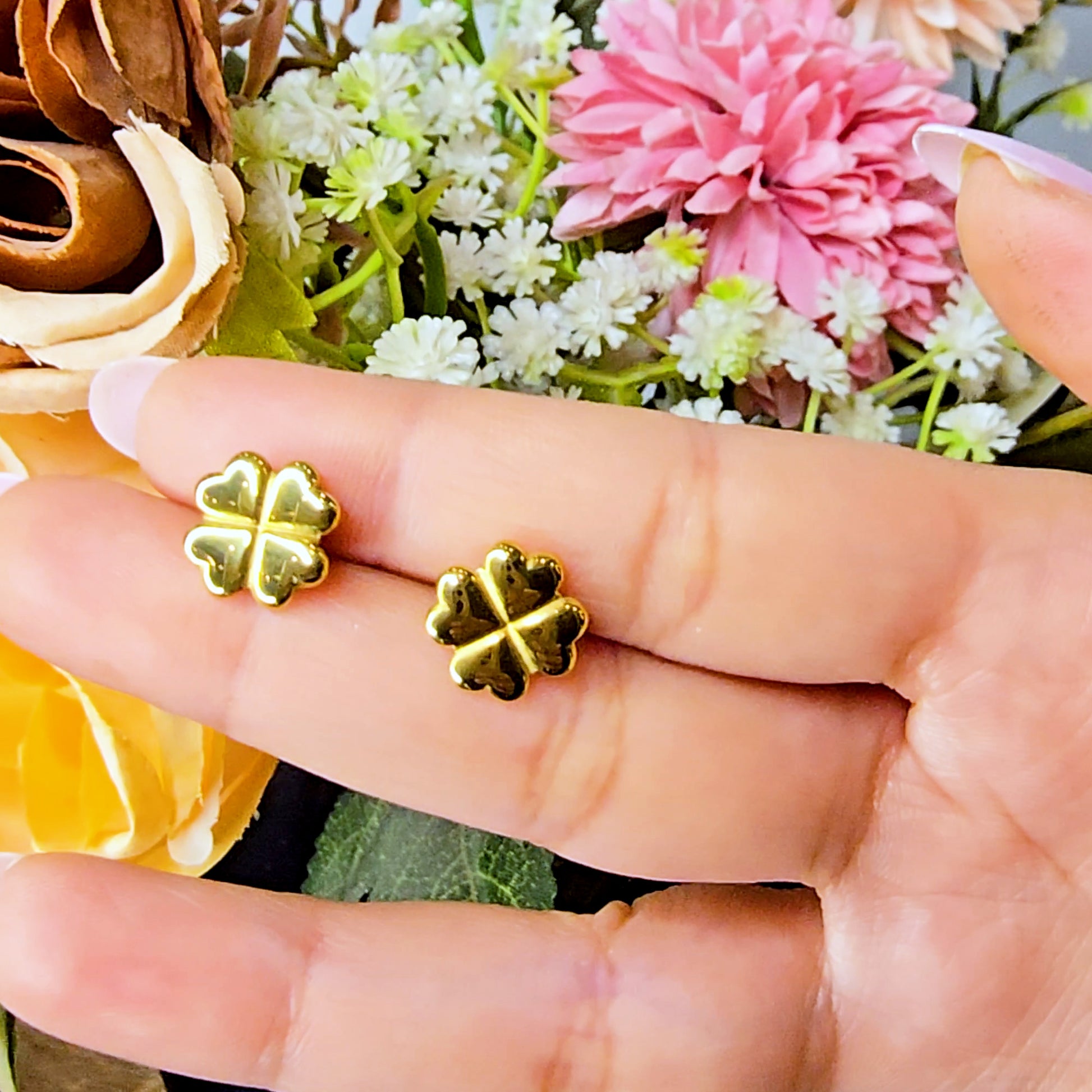 Hand holding a pair of gold clover earrings to demonstrate their reflective shine and petite size.