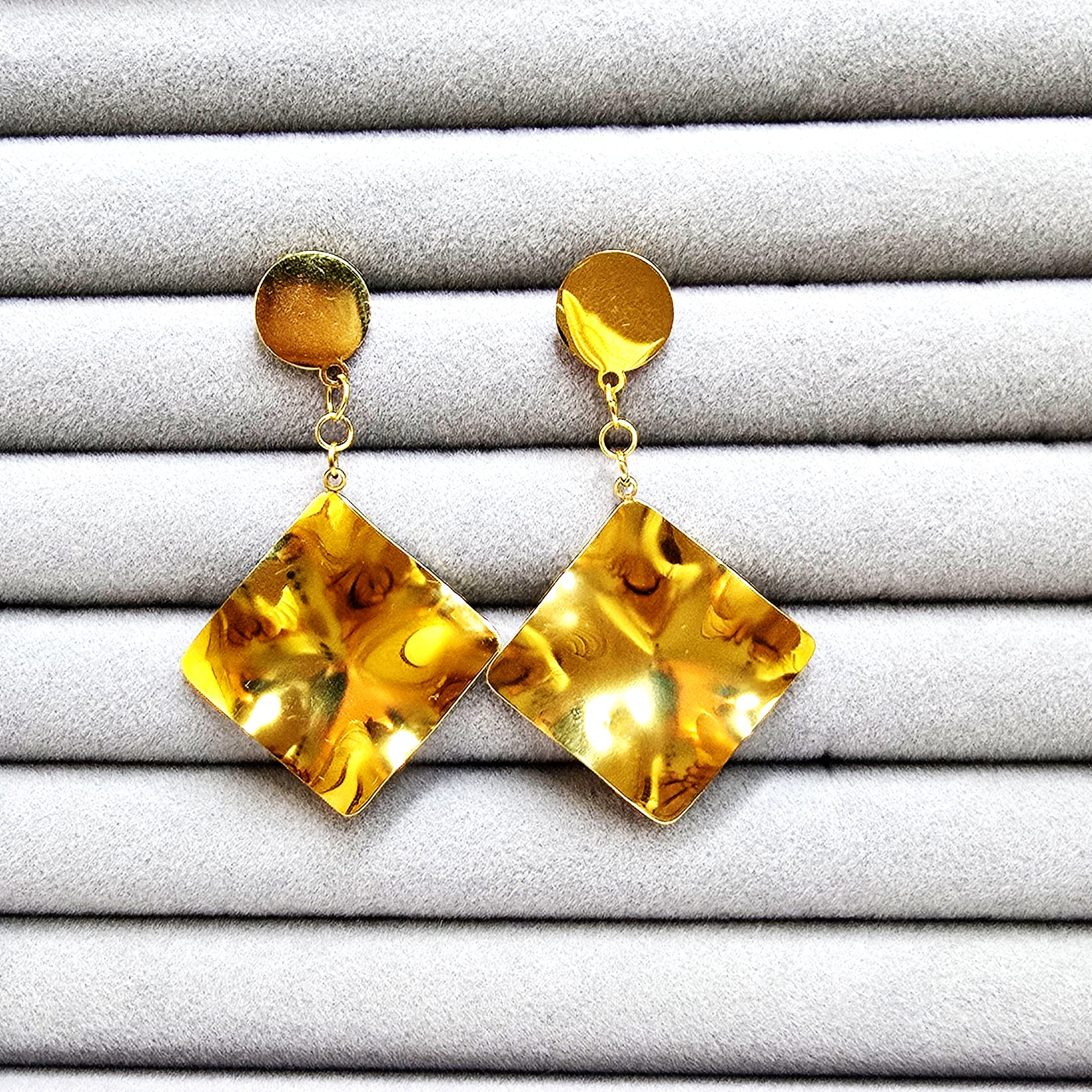 Pair of gold-plated liquid gold square drop earrings with a wavy, hammered texture on a grey velvet jewelry tray.