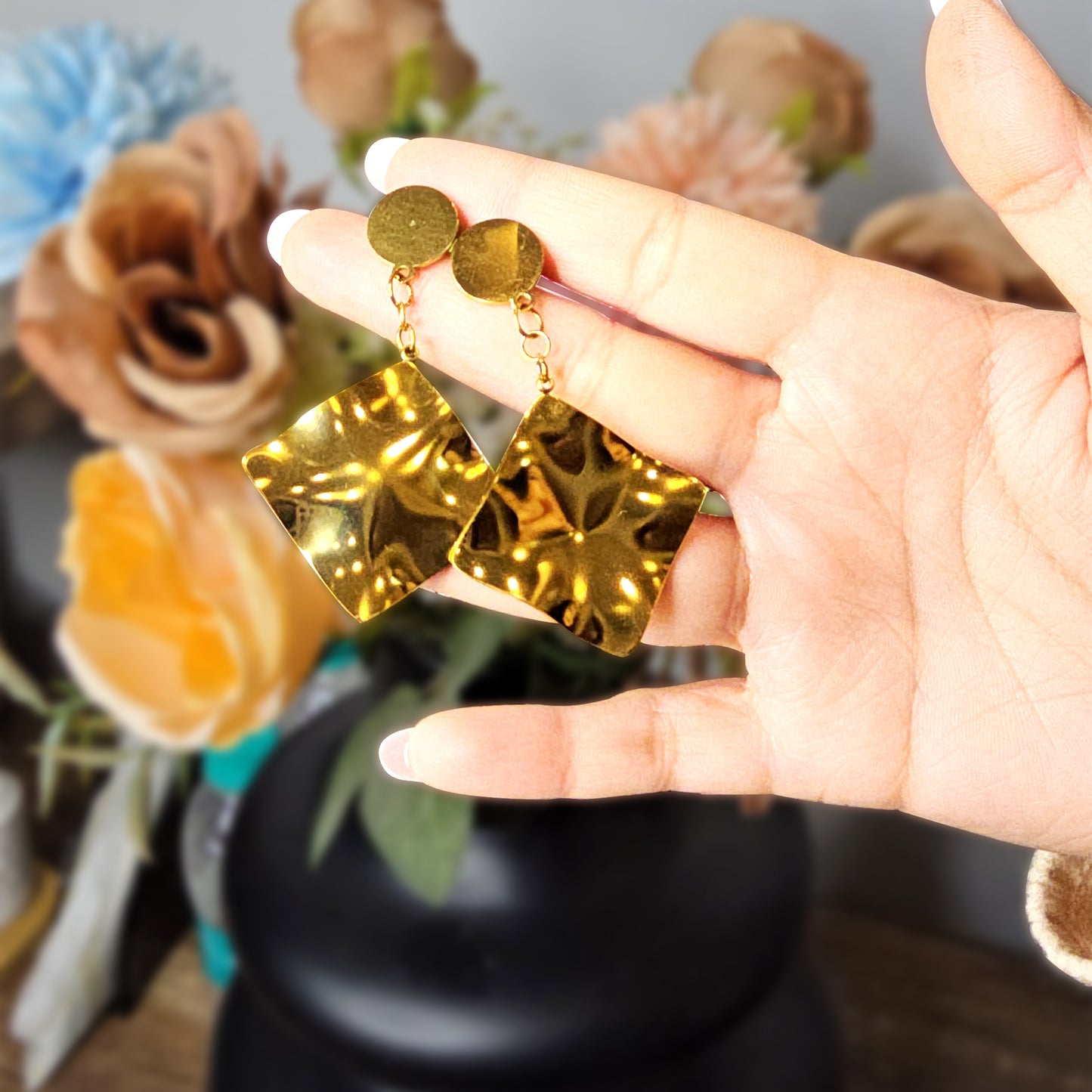 Hand holding two large gold-toned molten metal drop earrings to demonstrate their reflective shine and sculptural scale.