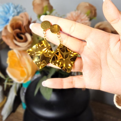 Hand holding two large gold-toned molten metal drop earrings to demonstrate their reflective shine and sculptural scale.