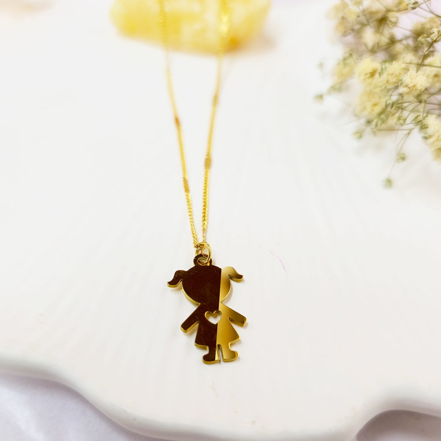 Close-up of gold-plated little girl silhouette necklace on a white background with floral detail.