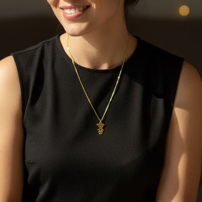 Model wearing the gold little girl necklace against a black sleeveless top, showcasing the length and scale.