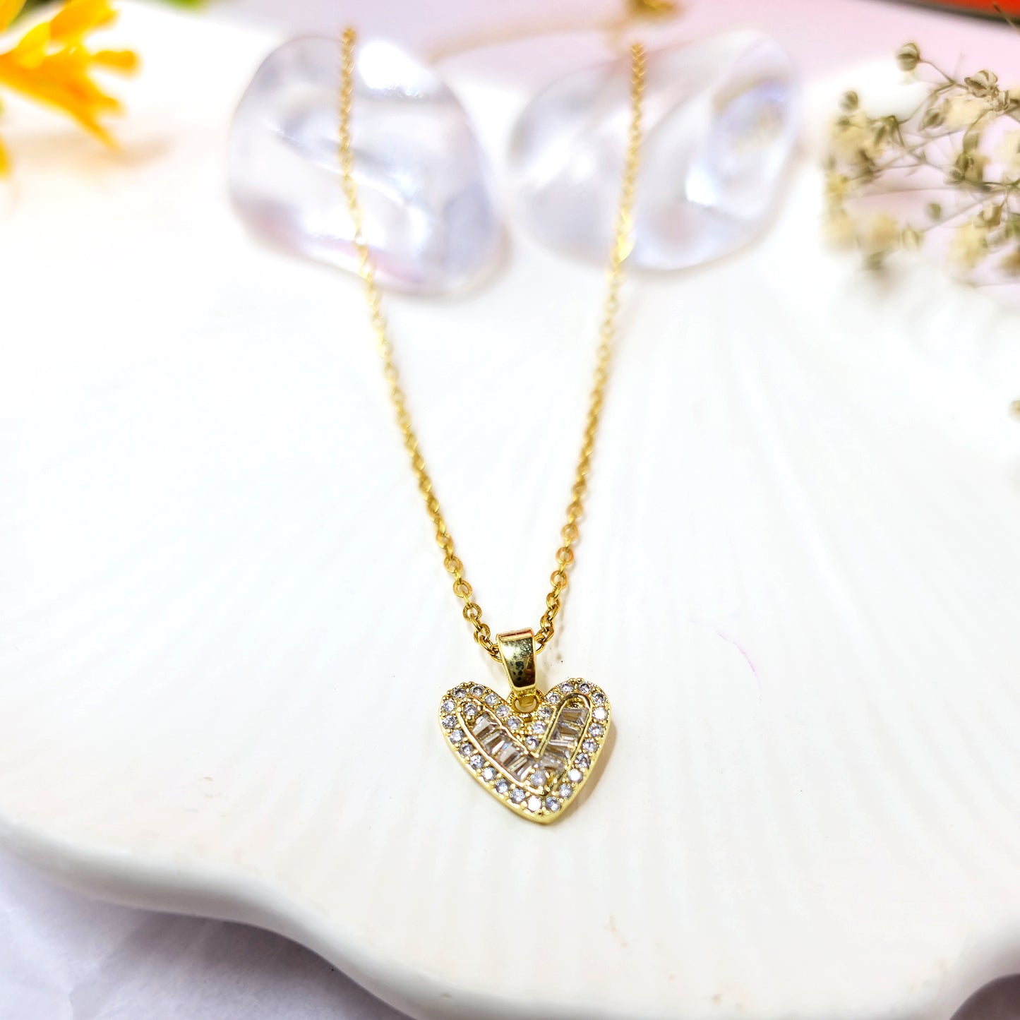 Gold-plated heart pendant necklace with baguette and pavé crystals on a white scalloped dish.