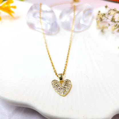 Gold-plated heart pendant necklace with baguette and pavé crystals on a white scalloped dish.
