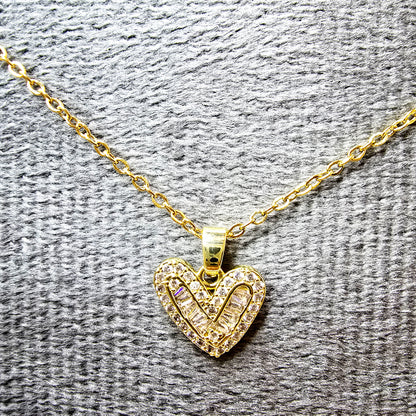 Close-up of the crystal-set heart pendant showing baguette and round crystal arrangement on a grey texture.