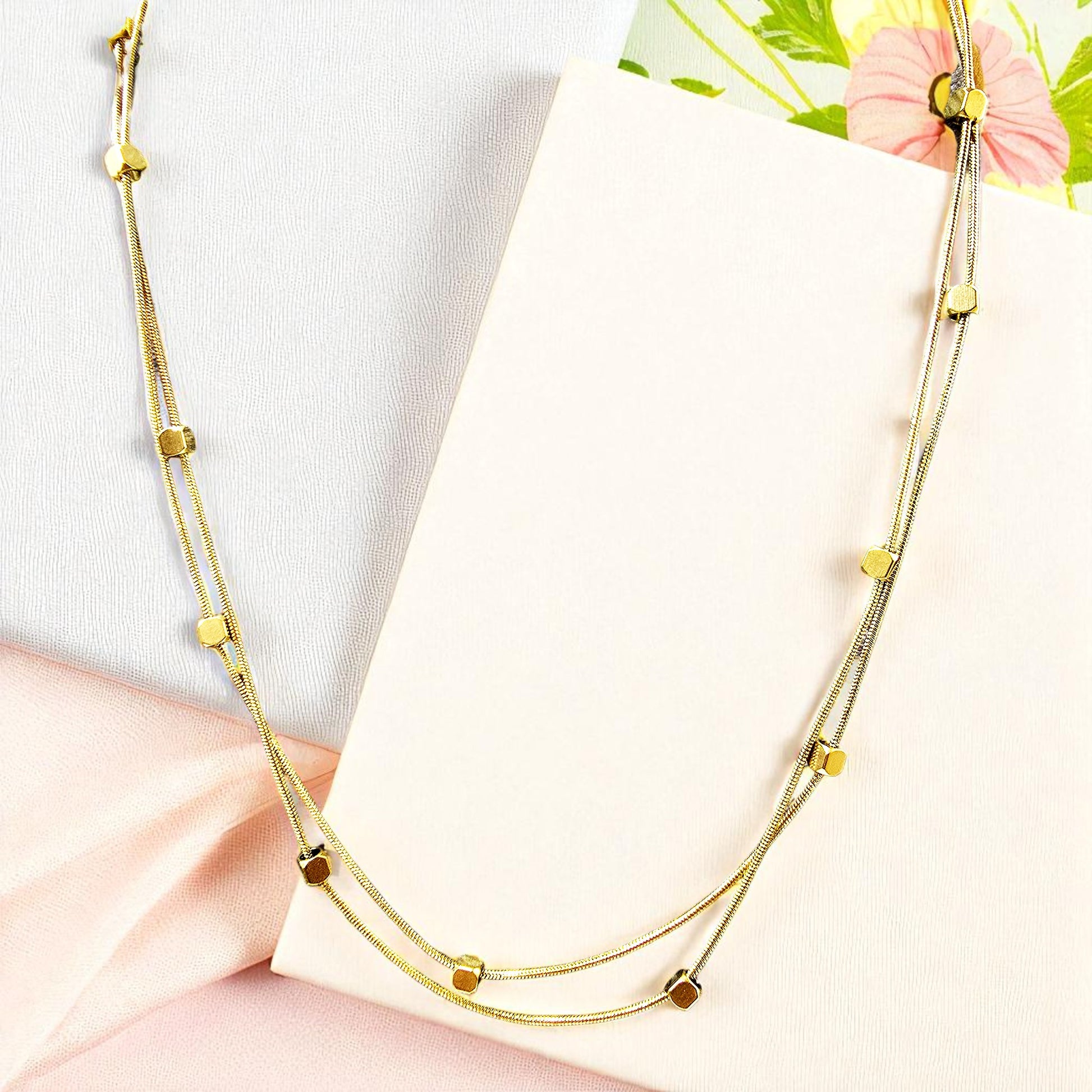 Flatlay of Loose Pixel Chain on textured fabric – gold-toned layered necklace with geometric beads