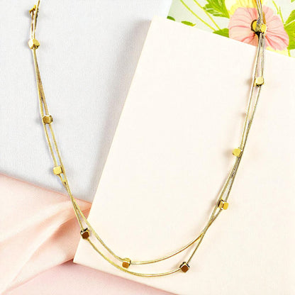 Flatlay of Loose Pixel Chain on textured fabric – gold-toned layered necklace with geometric beads