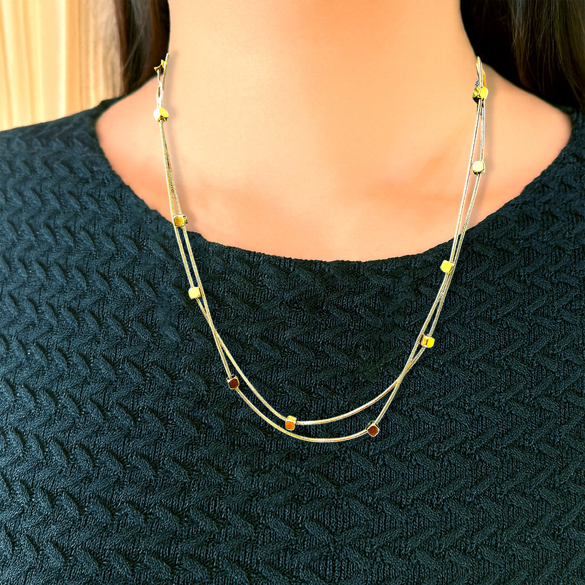 Model wearing Loose Pixel Chain – gold-toned double-layer necklace featuring geometric cube beads, styled over a black textured top for a minimalist look