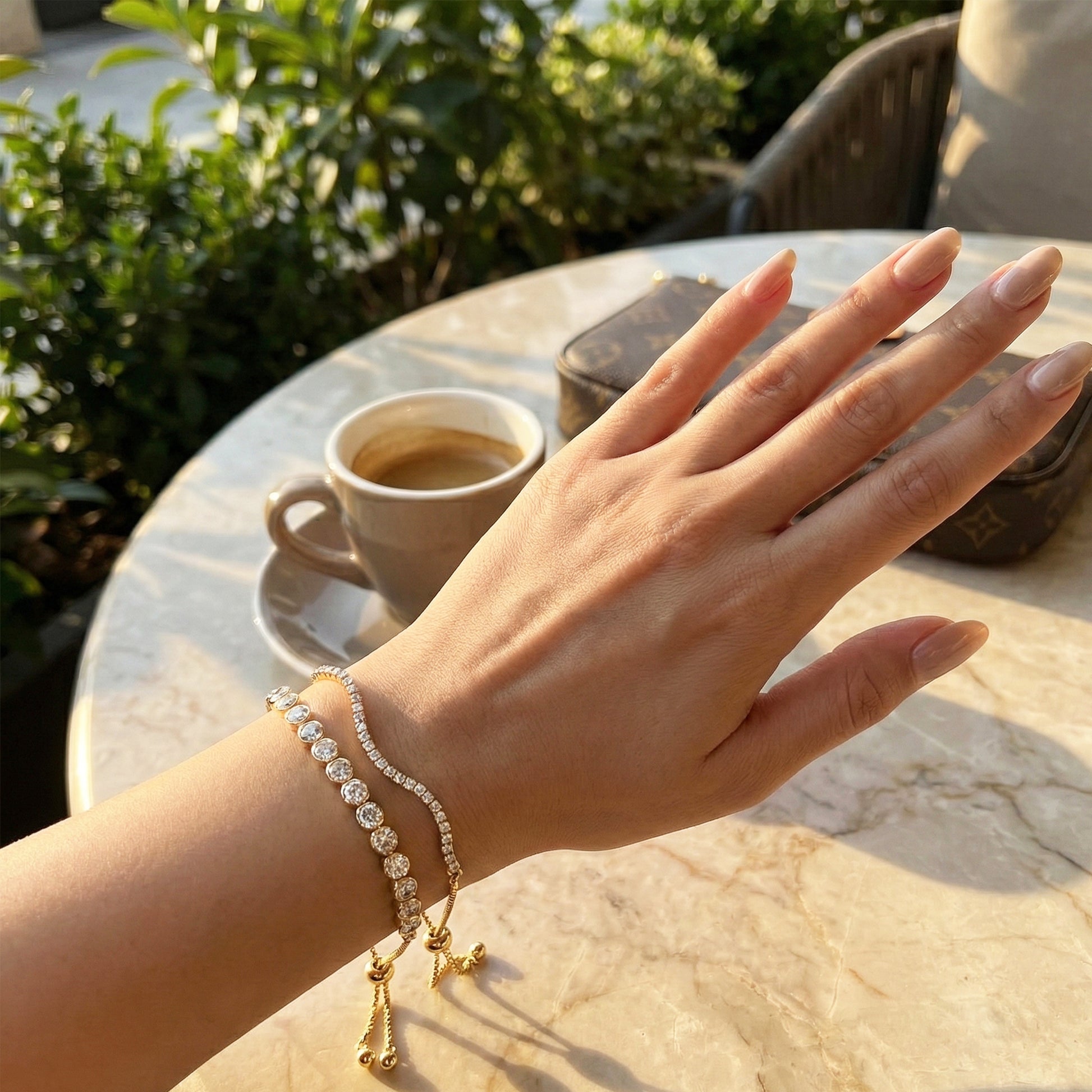 Woman's hand wearing double-layered gold crystal tennis bracelet with adjustable slider.