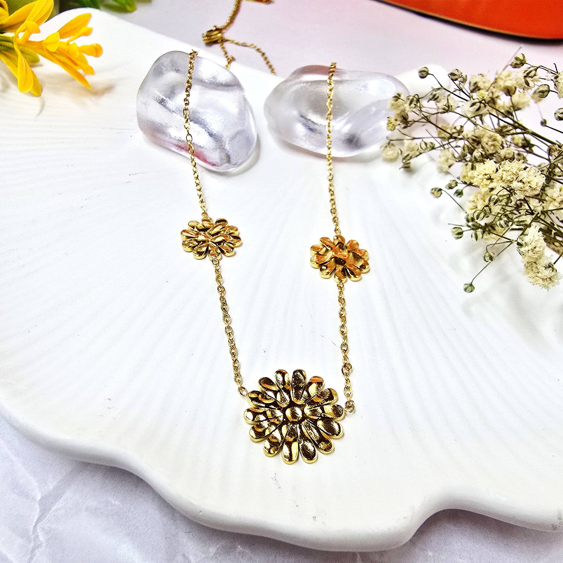 Gold-plated marigold flower station necklace with three charms on a white textured display.