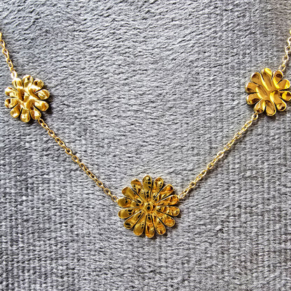 Close-up of the textured gold marigold flower charms on a grey fabric background.