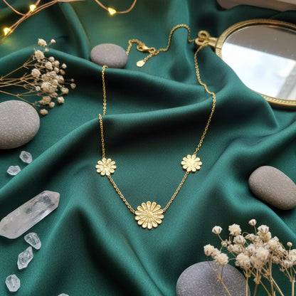Three-charm gold marigold necklace styled on a dark green silk fabric with crystals and natural stones.