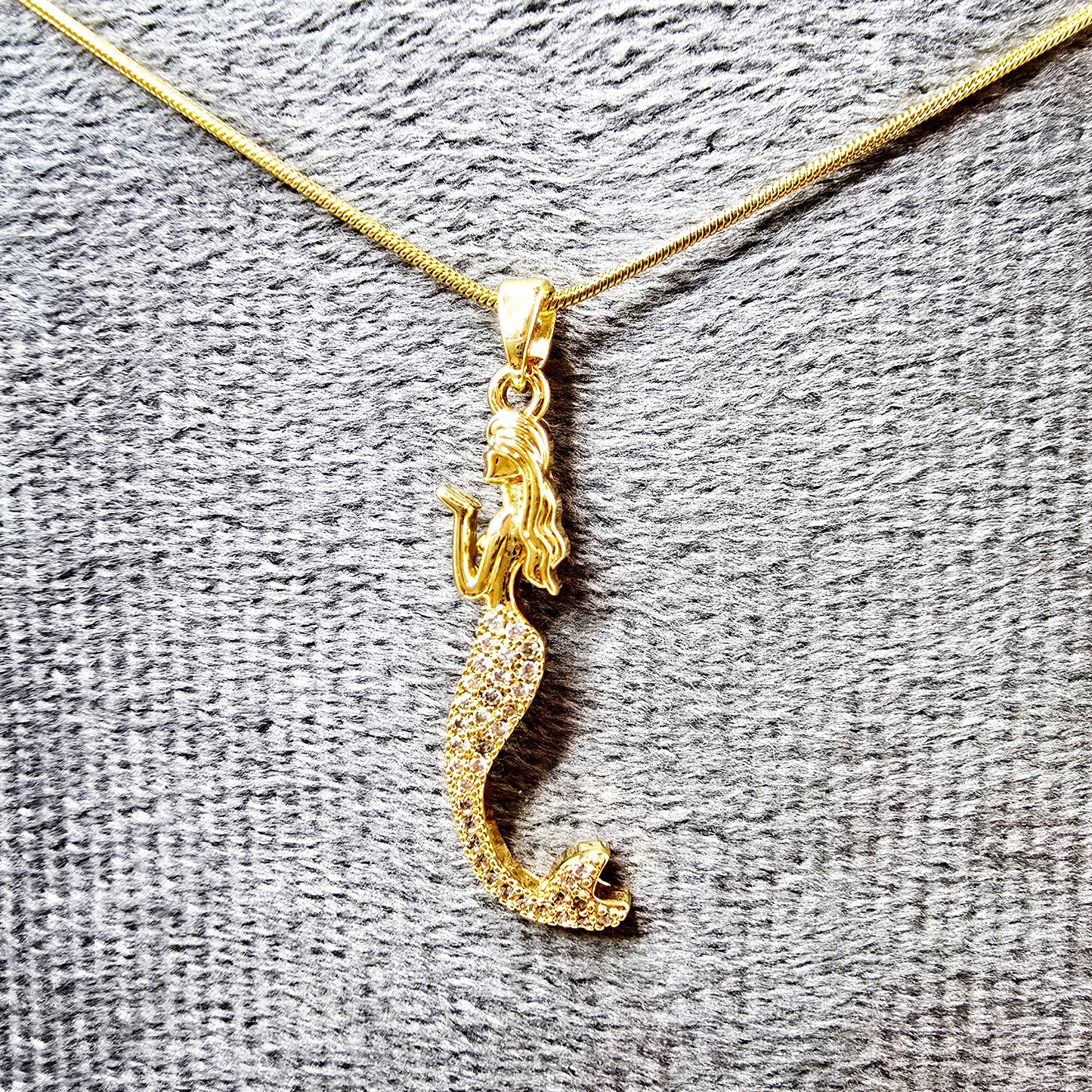 Sparkling mermaid pendant necklace with crystal tail on a grey textured background.