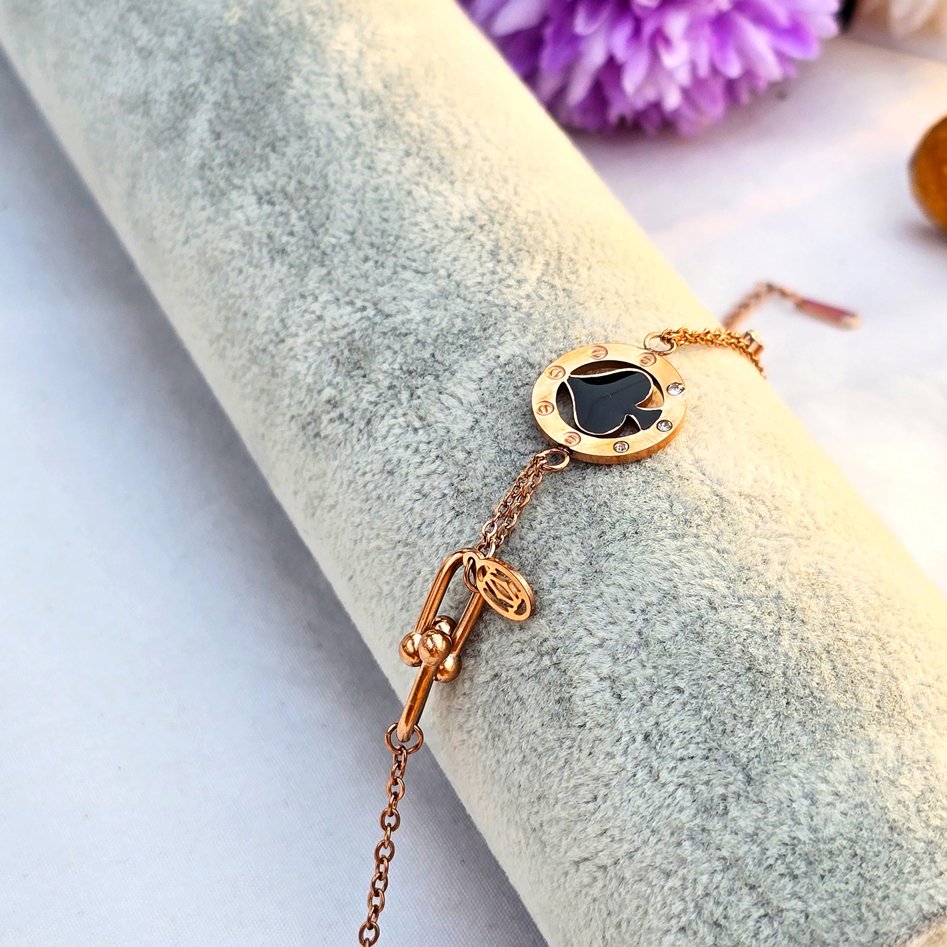 Studio shot of a gold chain bracelet with a single black enamel spade charm.