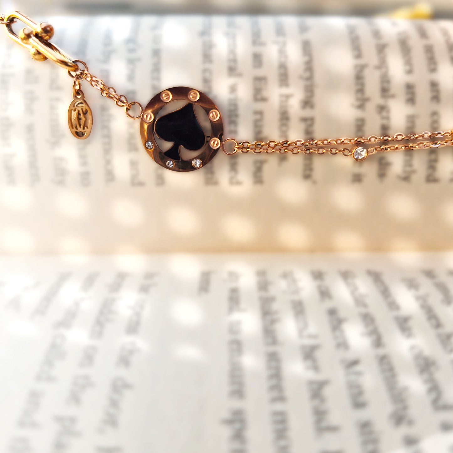 Close-up detail of the black spade charm resting on a book, highlighting the glossy enamel finish.