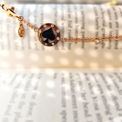 Close-up detail of the black spade charm resting on a book, highlighting the glossy enamel finish.