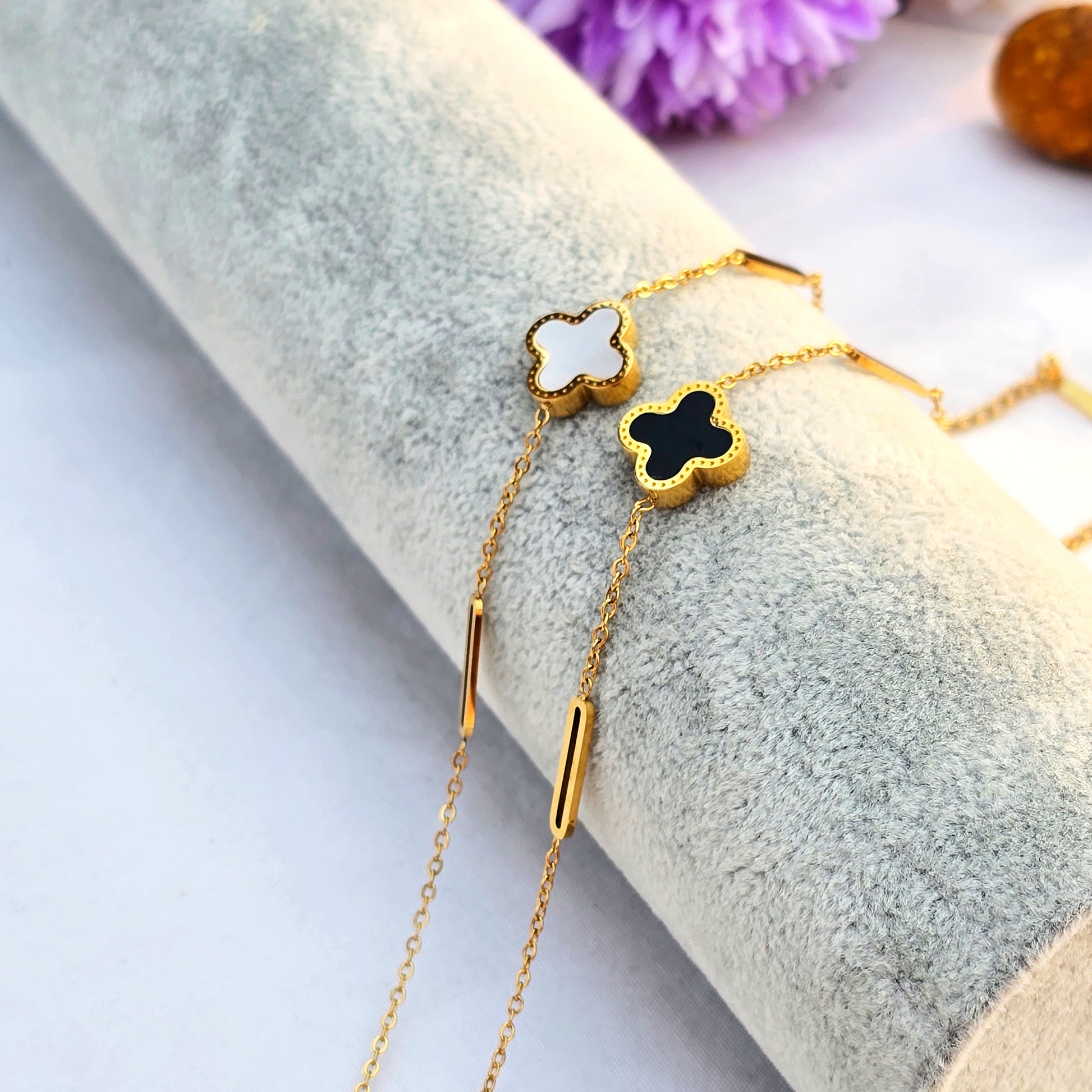 Side-by-side view of black and white clover bracelets featuring unique gold station chains.