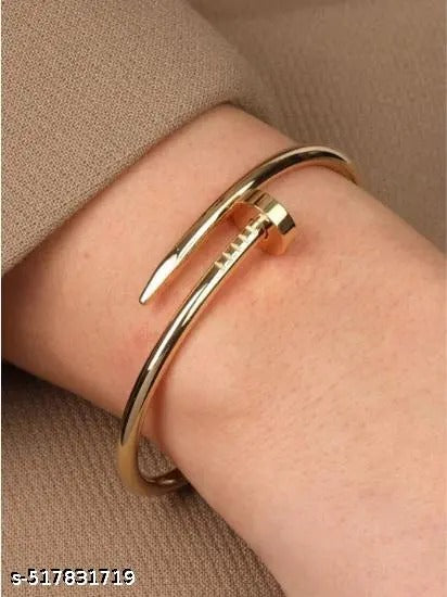 Nail-inspired gold bangle styled on model’s wrist against beige outfit